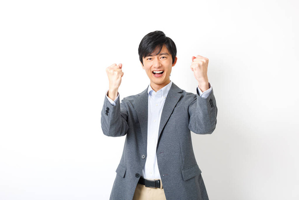 Young Japanese man in office attire showing cheering gesture on white background - Photo, Image