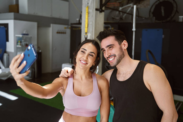 brunette fitness couple taking a selfie with their cell phone smiling after finishing their workout - Photo, Image