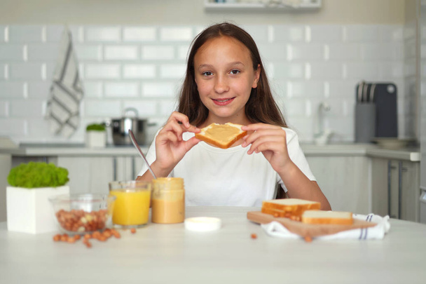 A girl in a good mood making a peanut butter sandwich in the kitchen. High quality photo - Φωτογραφία, εικόνα