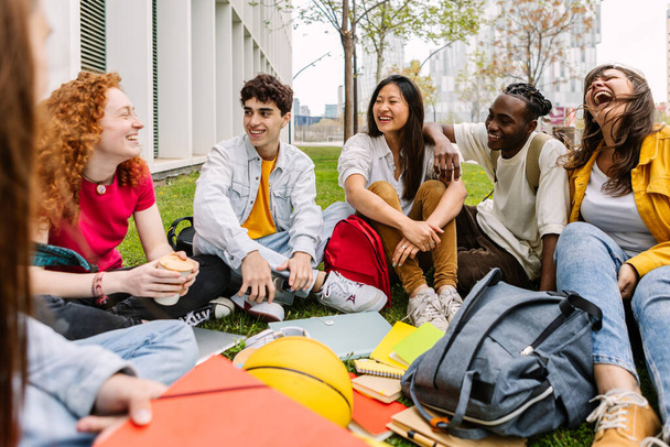 Концепция студенческой дружбы с одноклассниками, сидящими вместе на траве в университетском парке колледжа. Тысячелетние люди веселятся на улице. Молодежь и образование. - Фото, изображение