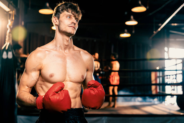 ボクシングの戦闘機の無表情なポーズ、守備の姿勢で赤い手袋を身に着けている白人男性のボクサーは、背景にリングやボクシング機器とジムで戦うとパンチする準備ができています。インペトゥス - 写真・画像