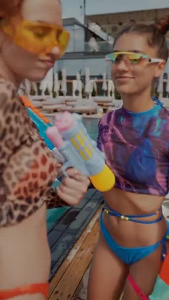 Der Anblick von Mädchen in lebhaften Badeanzügen, die mit Wasserpistolen in der Nähe des Pools tanzen, ist ein entzückendes Spektakel. Hochwertiges 4k Filmmaterial - Filmmaterial, Video
