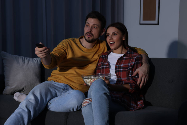 Couple watching TV at home in evening. Man changing channels with remote control - Foto, immagini