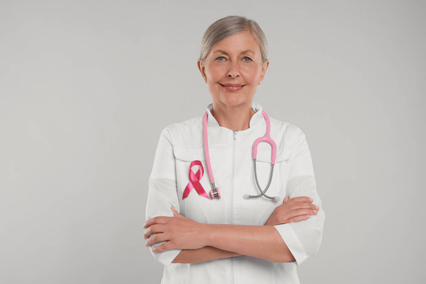 Doctor with pink ribbon and stethoscope on light grey background. Breast cancer awareness - Foto, immagini