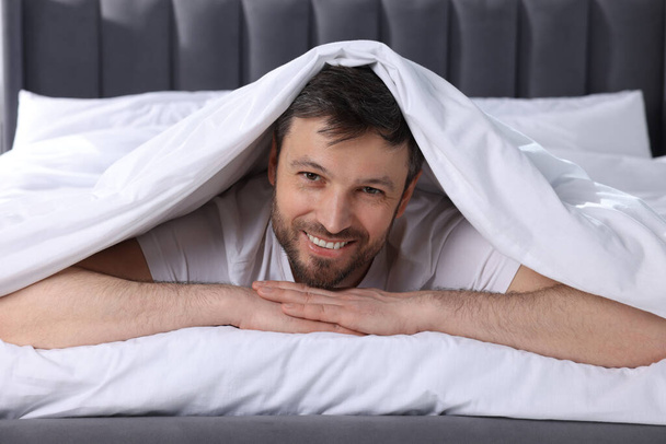 Happy man wrapped in blanket on soft bed - Фото, изображение