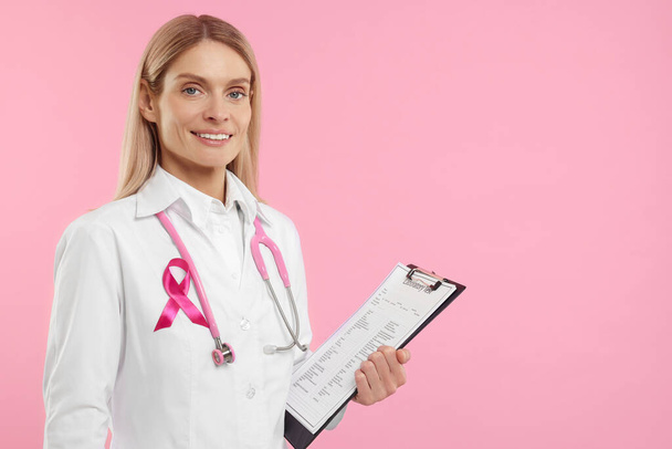Doctor with pink ribbon, clipboard and stethoscope on color background, space for text. Breast cancer awareness - Foto, Bild