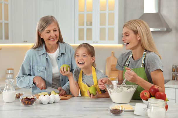 Three generations. Happy grandmother, her daughter and granddaughter cooking together in kitchen - Photo, Image