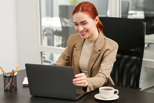 Happy woman working with laptop at black desk in office - Fotó, kép