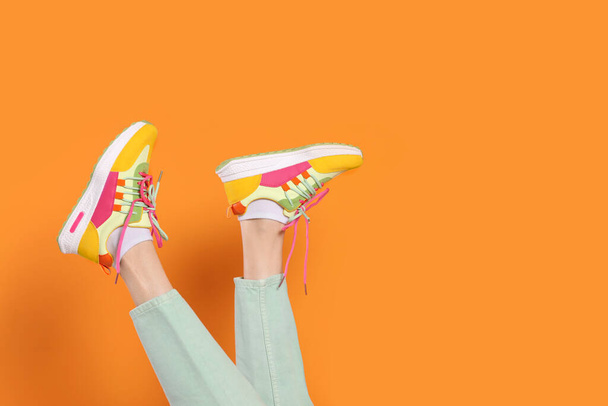 Woman wearing pair of new stylish sneakers on orange background, closeup. Space for text - Fotografie, Obrázek