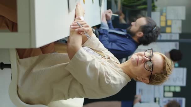 Vertikale Aufnahme einer kurzhaarigen Geschäftsfrau mit Brille, die am Schreibtisch sitzt und während ihrer Arbeit im Büro für die Kamera posiert - Filmmaterial, Video