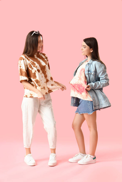 Stylish young women in tie-dye t-shirts on pink background - 写真・画像