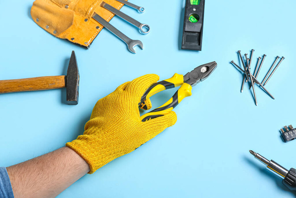 Mužská ruka v rukavicích drží kleště v blízkosti různých nástrojů na modrém pozadí - Fotografie, Obrázek