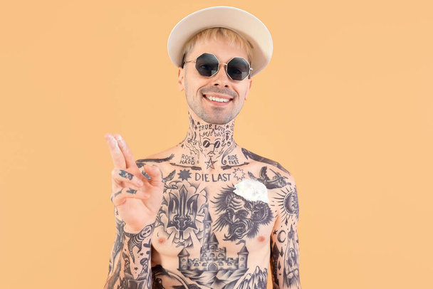 Татуированный мужчина наносит крем от загара на бежевый фон - Фото, изображение
