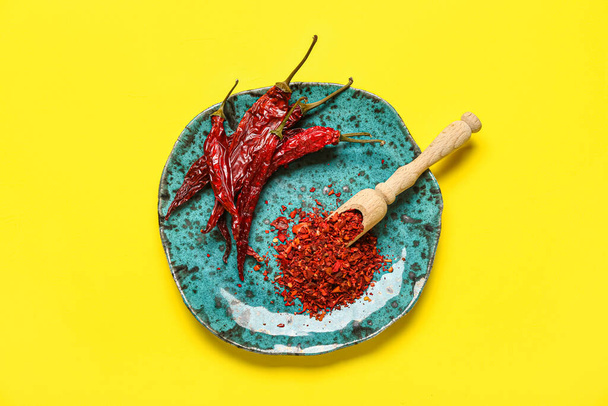 Plate with dry chili and ground  peppers on yellow background - Photo, image