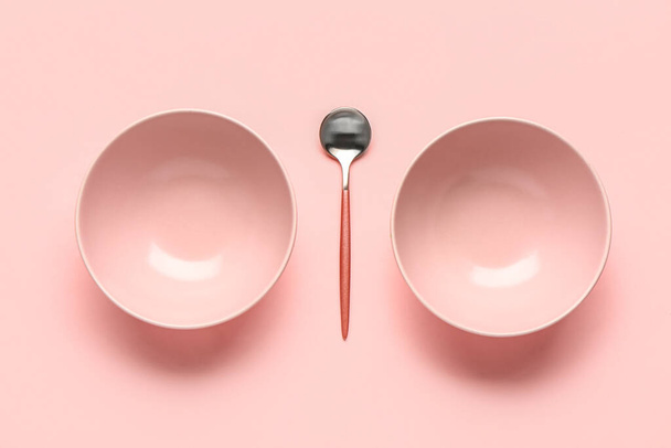 Composición con cuencos limpios y cuchara sobre fondo rosa - Foto, Imagen