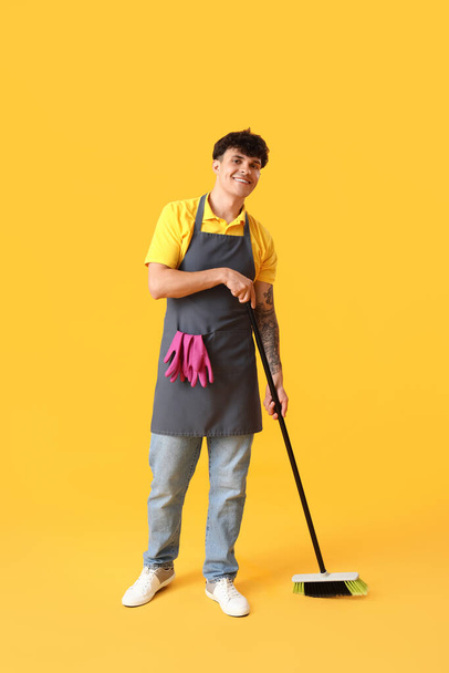 Male janitor with broom on yellow background - Fotoğraf, Görsel