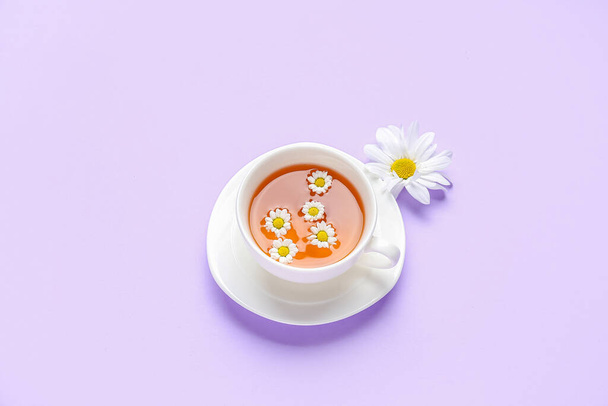 Cup of natural chamomile tea with flower on lilac background - Foto, imagen