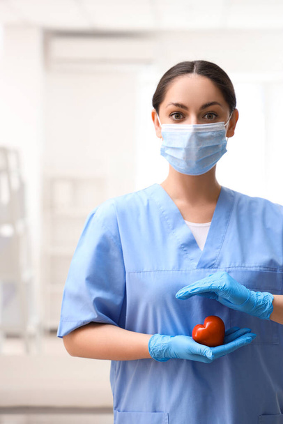 Γυναικεία νοσοκόμα με ιατρική μάσκα και καρδιά στην κλινική - Φωτογραφία, εικόνα