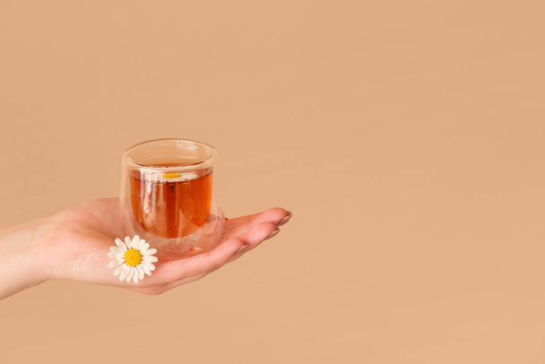 Mão feminina com xícara de chá de camomila perto da parede bege - Foto, Imagem