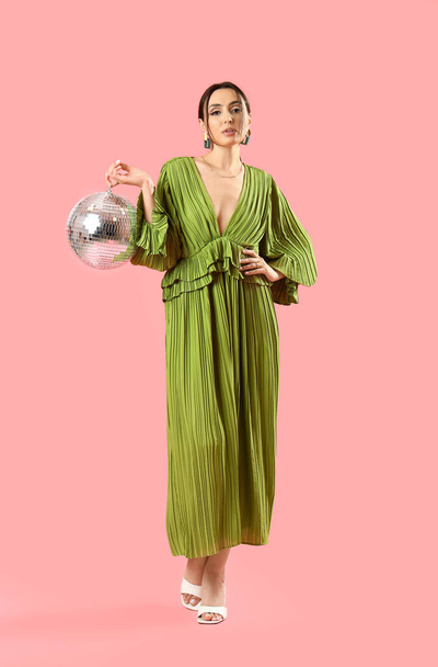 Μοντέρνα όμορφη γυναίκα σε κομψό πράσινο φόρεμα με μπάλα ντίσκο ποζάρουν σε ροζ φόντο - Φωτογραφία, εικόνα