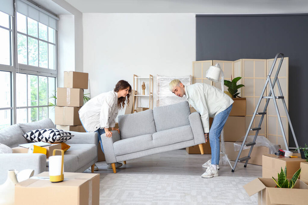 Young couple carrying sofa in room on moving day - Fotoğraf, Görsel