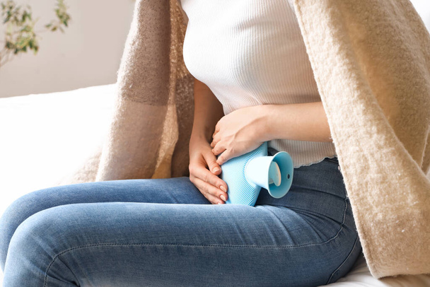 Young woman with hot water bottle having menstrual cramps in bedroom, closeup - Foto, Imagem