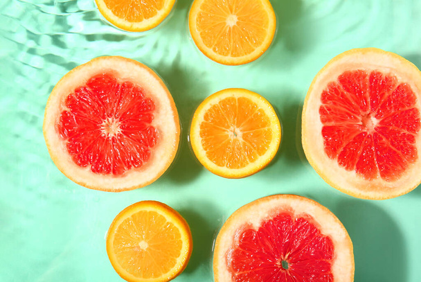 Slices of fresh orange and grapefruit in water on turquoise background - Photo, Image