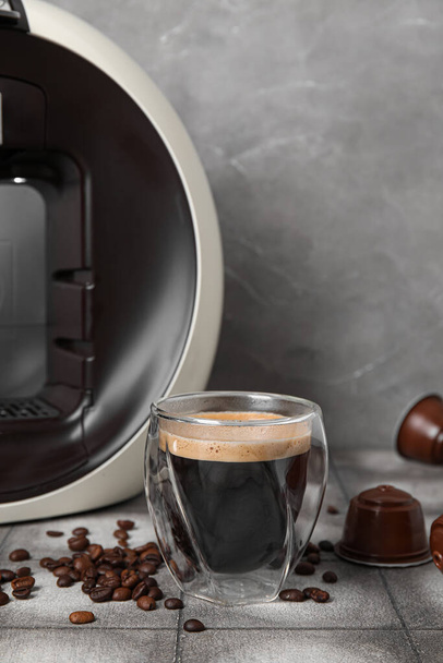 Glas heerlijke espresso, capsule koffiezetapparaat, peulen en bonen op grijze grunge tafel - Foto, afbeelding