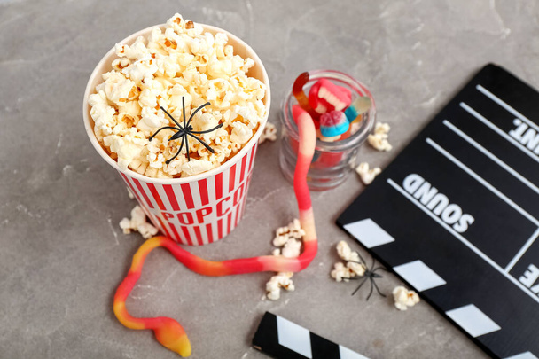Bucket with tasty popcorn, clapperboard and candies on grey background, closeup. Halloween celebration - Photo, Image
