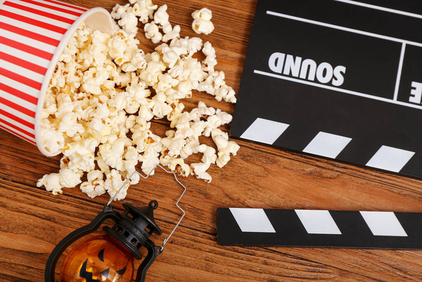 Kbelík s chutným popcornem, lucernou a prknem na dřevěném pozadí, detailní záběr. Halloween oslava - Fotografie, Obrázek