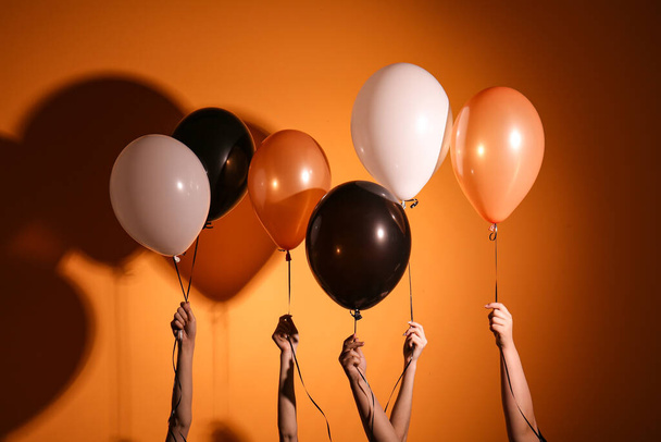Female hands with different Halloween balloons on orange background - Fotografie, Obrázek