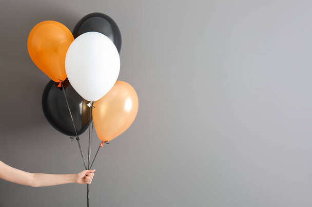 Female hand with different Halloween balloons on grey background - Photo, image