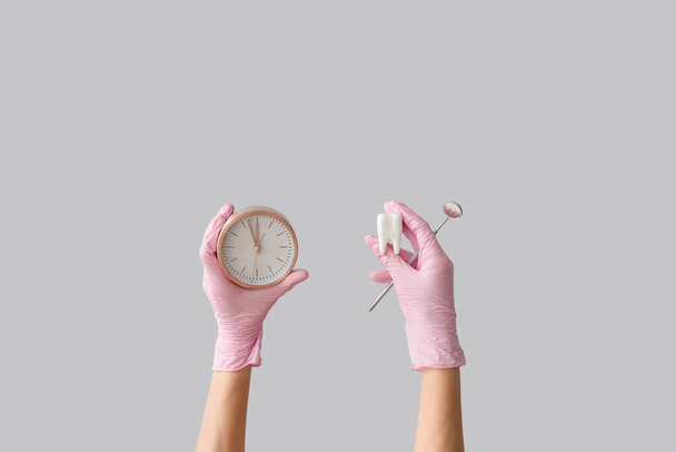 Female doctor's hands with dental mirror, teeth model and clock on grey background - Foto, afbeelding