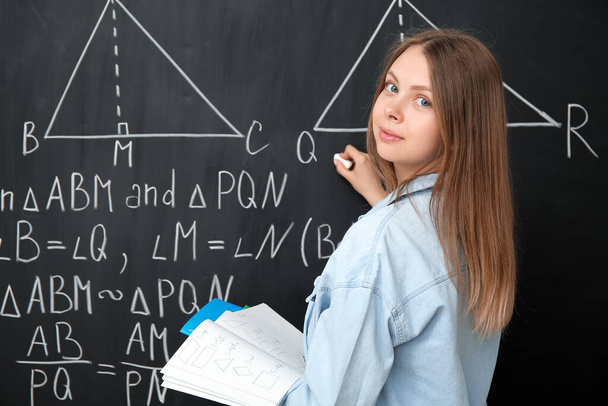 Jeune professeur de mathématiques avec copybooks écrit sur tableau noir en classe - Photo, image