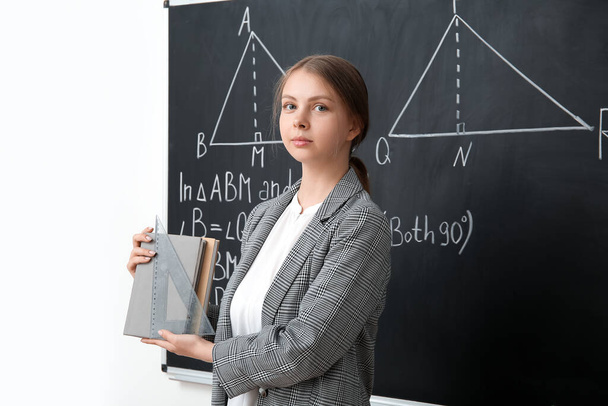 Jeune professeur de mathématiques avec des livres près du tableau noir en classe - Photo, image