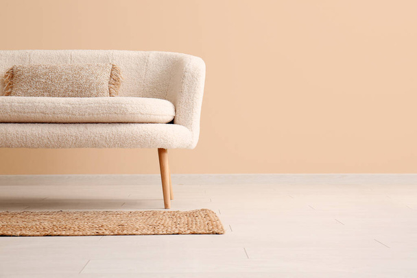 Hangulatos fehér kanapé párnával és szőnyeggel a bézs fal közelében - Fotó, kép