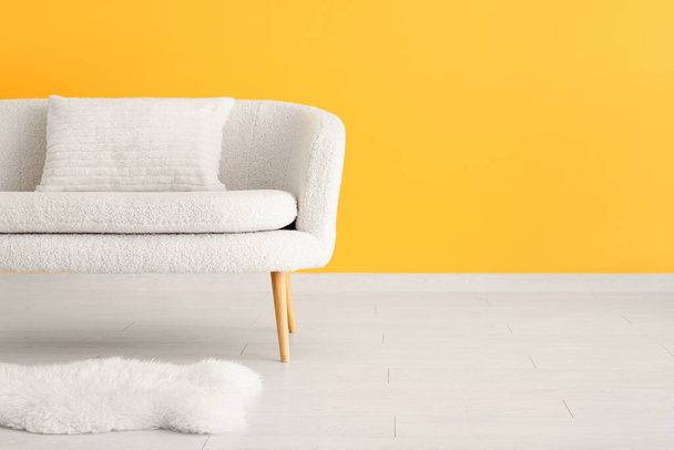Άνετο λευκό καναπέ με μαξιλάρι και χαλί κοντά σε κίτρινο τοίχο - Φωτογραφία, εικόνα