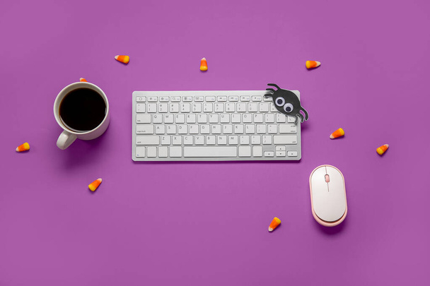 Kompozycja z nowoczesną klawiaturą komputerową, myszą, filiżanką kawy i smacznymi kukurydzianymi cukierkami na Halloween na fioletowym tle - Zdjęcie, obraz