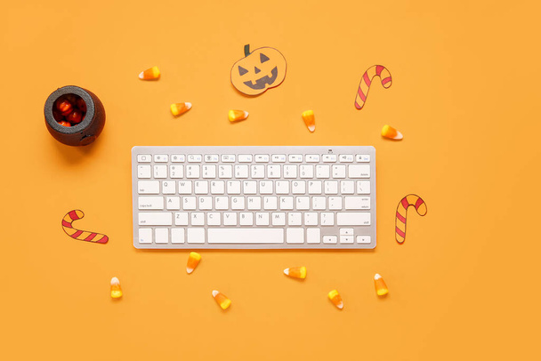 Composición con teclado de computadora moderno y sabrosos callos de caramelo para Halloween sobre fondo naranja - Foto, Imagen