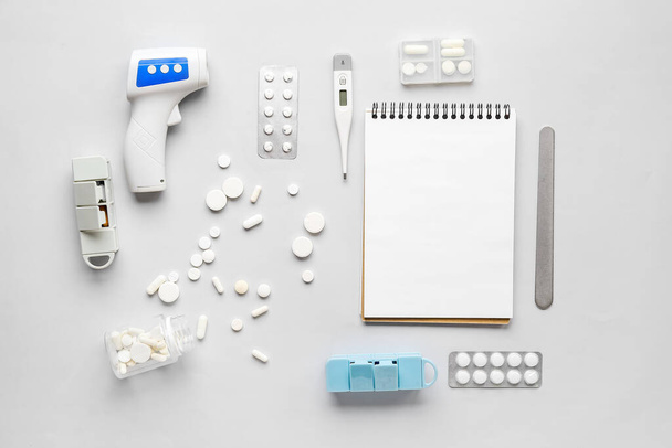 Složení s pilulkami, teploměrem, stetoskopem a notebookem na šedém pozadí - Fotografie, Obrázek