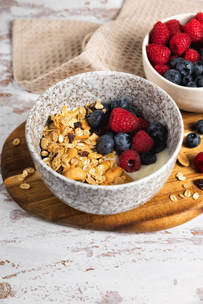 Cuenco de granola de avena casera con yogur y bayas frescas en una mesa de madera rústica. Desayuno saludable con nueces y pasas - Foto, imagen