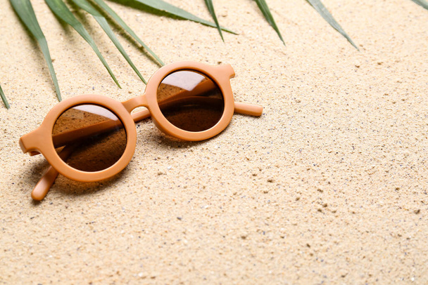 Lunettes de soleil féminines élégantes et feuille de palmier sur fond de sable - Photo, image