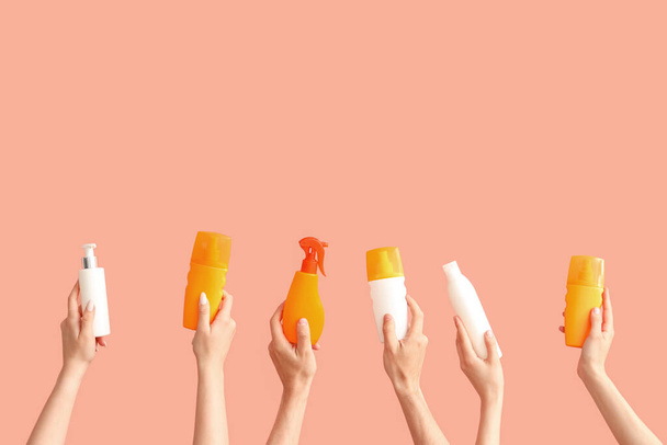 Mains féminines avec des bouteilles de crème solaire sur fond de couleur - Photo, image