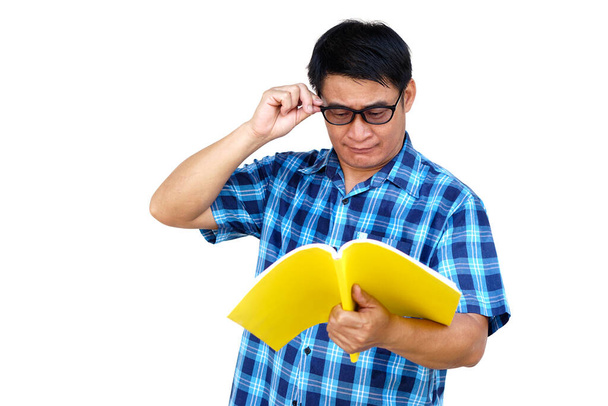 Aziatische man van middelbare leeftijd draagt bril is het lezen van boek, geïsoleerd op witte achtergrond. Concept, lezen voor kennis of plezier. Hobby en relax tijd. Een slechtziende man leest boek..      - Foto, afbeelding