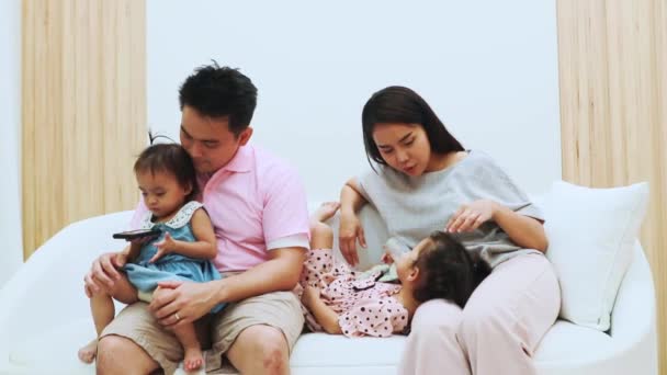 Gelukkige Aziatische familie: Ouders zitten en zorgen voor hun kleine dochter op de bank, liefdevol en liefdevol in een warm huis. - Video