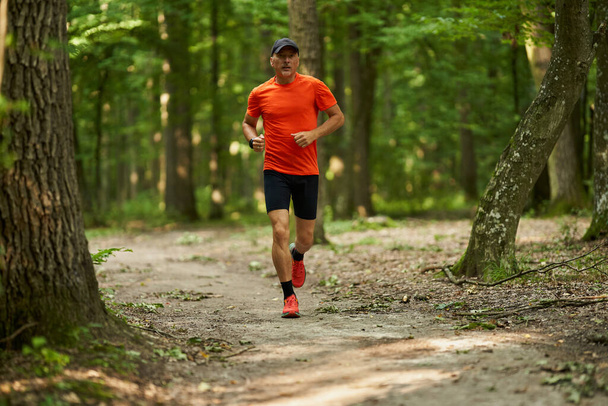 Un homme caucasien faisant du jogging sur un sentier de course à travers la forêt - Photo, image