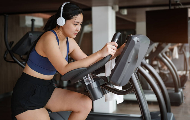 Young woman in sportswear, burning calories, cycling bikes in gym. - Photo, Image