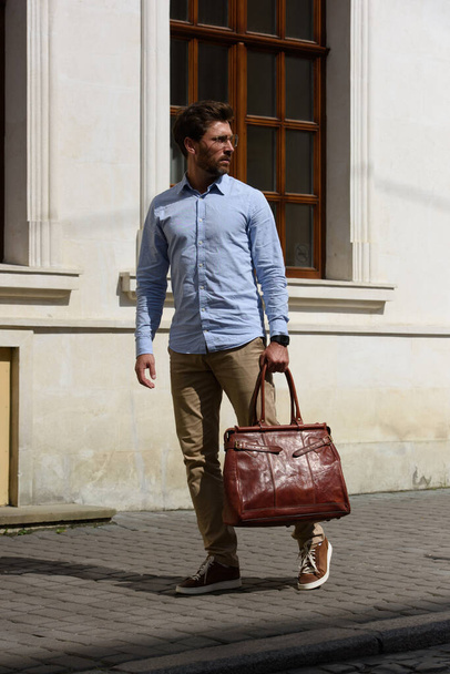 Όμορφος επιχειρηματίας περπατά στο δρόμο, με δερμάτινη τσάντα πολυτελείας. Μοντέρνο στυλ. Φωτογραφία δρόμου - Φωτογραφία, εικόνα