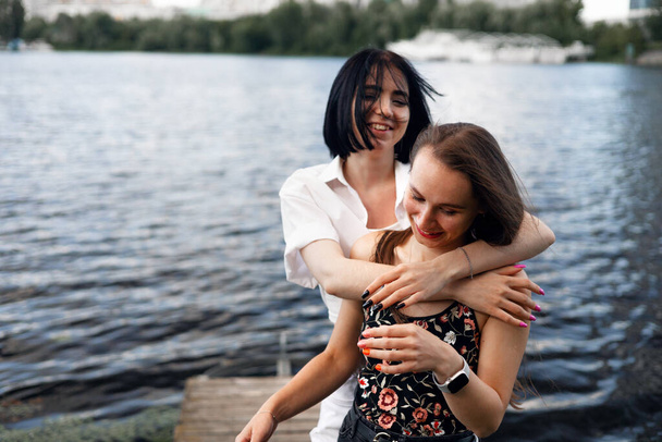 Két tinédzser lány ül egy mólón a folyóparton, és jól érzik magukat nyáron. boldog lány barátok pihentető szabadban tó közelében. - Fotó, kép