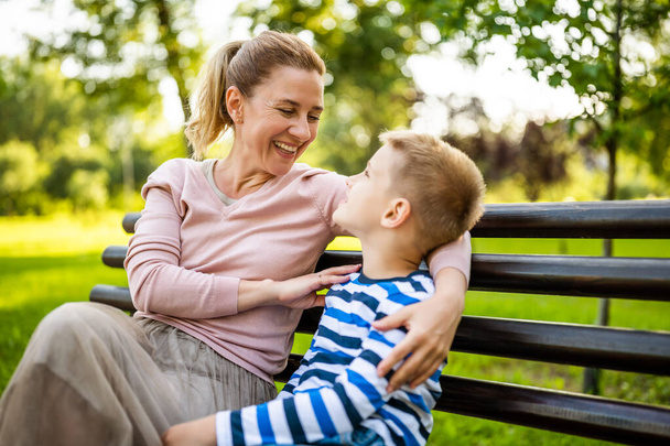 Mère heureuse est assise avec son fils sur le banc dans le parc. Ils s'amusent ensemble.. - Photo, image
